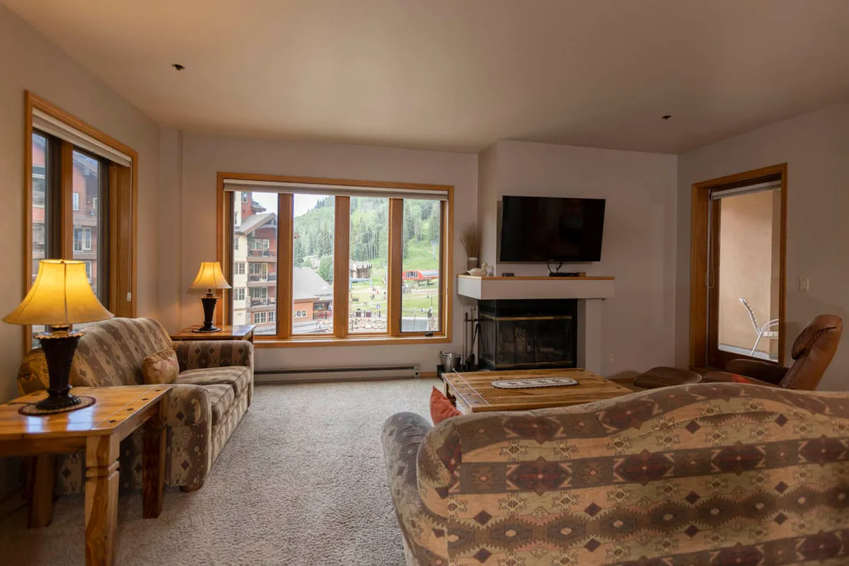 An inviting living area with comfortable seating grouped around a fireplace, complemented by large windows that frame the mountain landscape beyond. The room is designed for relaxation and togetherness, perfect for sharing stories or enjoying a game night.