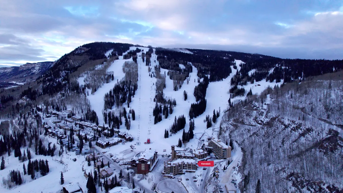 A panoramic view of snow-covered slopes, ski lifts, and residential buildings, set against a backdrop of majestic mountains. The scene captures both the thrill of outdoor mountain activities and the cozy, inviting feel of the village area.