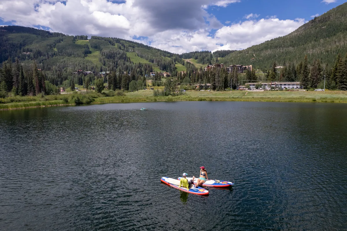 This image captures two people paddleboarding on a tranquil mountain lake, with serene water, dramatic mountain backdrops, and soft clouds in the sky. The scene exudes a sense of adventure and connection to nature, encapsulating the outdoor recreation options available nearby.