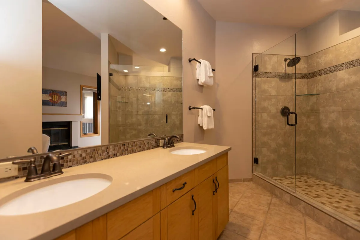 A spacious, elegant bathroom featuring a double sink vanity, glass shower enclosure, decorative tile backsplash, and a mirrored wall. The serene, spa-like setting is designed for relaxation and privacy.