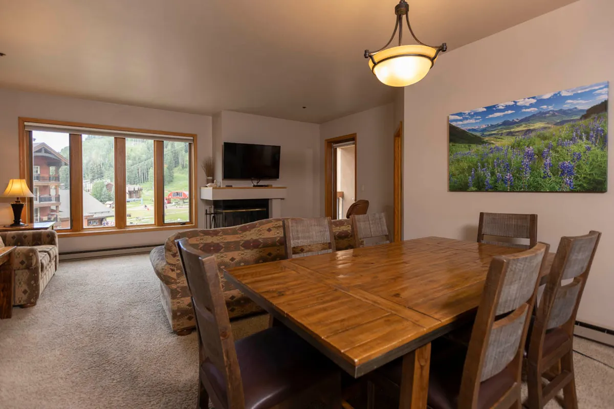 An open layout combining a dining table with nearby sofa, large window, and TV, all arranged to foster togetherness. The space is softly lit and designed for both meals and relaxation, seamlessly connecting the living and dining areas as described.
