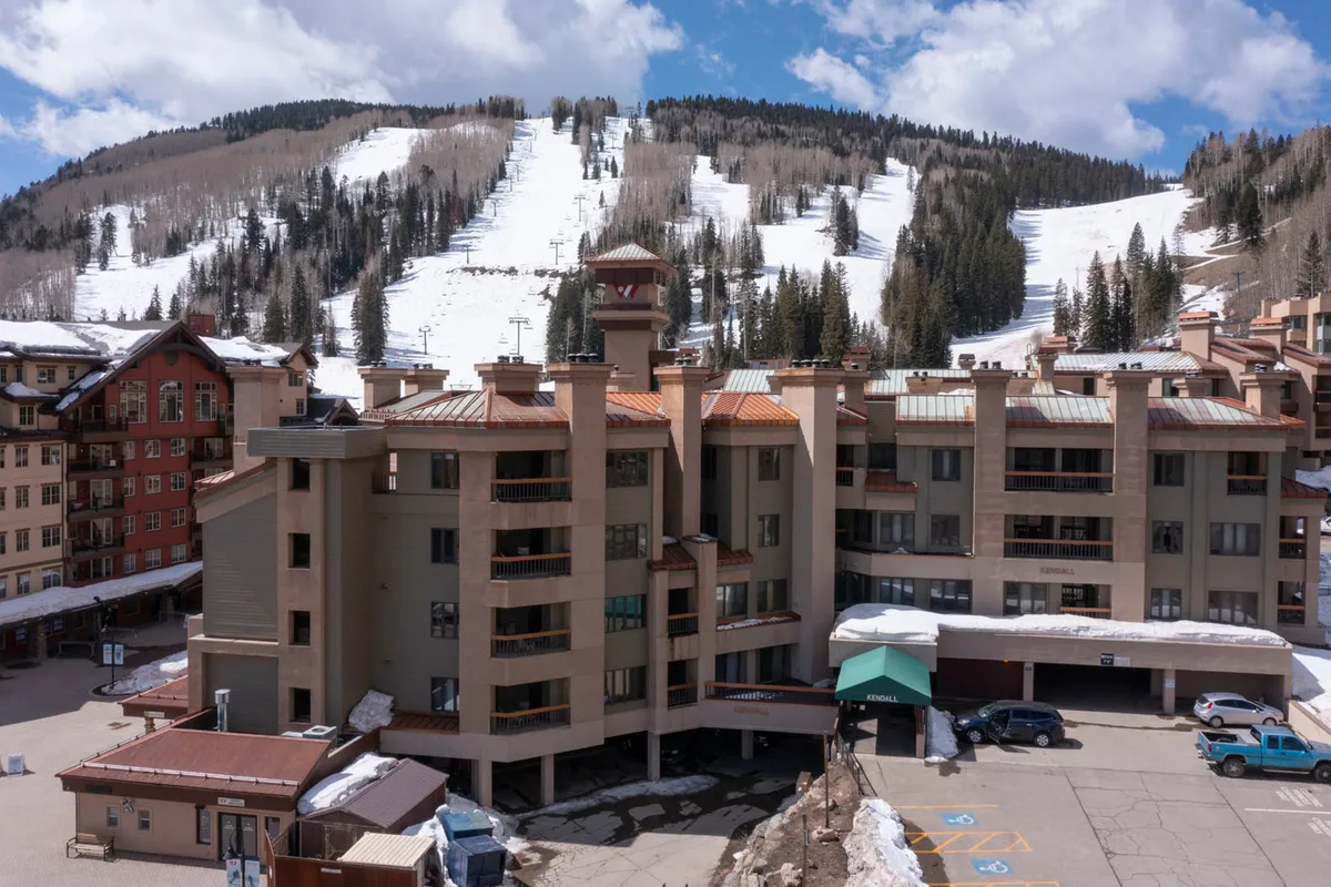 The exterior of the resort is set against ski slopes and a dramatic mountain backdrop, with architectural details and a visible parking area suggesting convenience and easy access. The environment hints at both adventurous mountain activities and cozy lodge life.