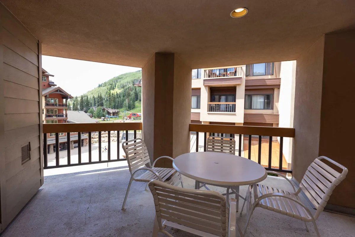 An inviting outdoor seating area on a balcony, overlooking beautiful mountain scenery. The setting exudes relaxation, with guests enjoying morning coffee or evening drinks while taking in the tranquil mountain views under an open sky.