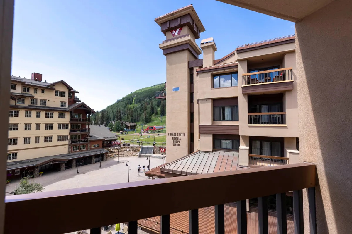 This image captures the lively village square with a clear view of the mountain backdrop and the inviting hotel architecture. People can be seen strolling, exploring local shops, and possibly enjoying outdoor dining, creating a vibrant and social scene.